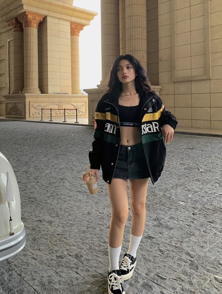 Woman in a crop top and denim skirt with a bomber jacket outdoors