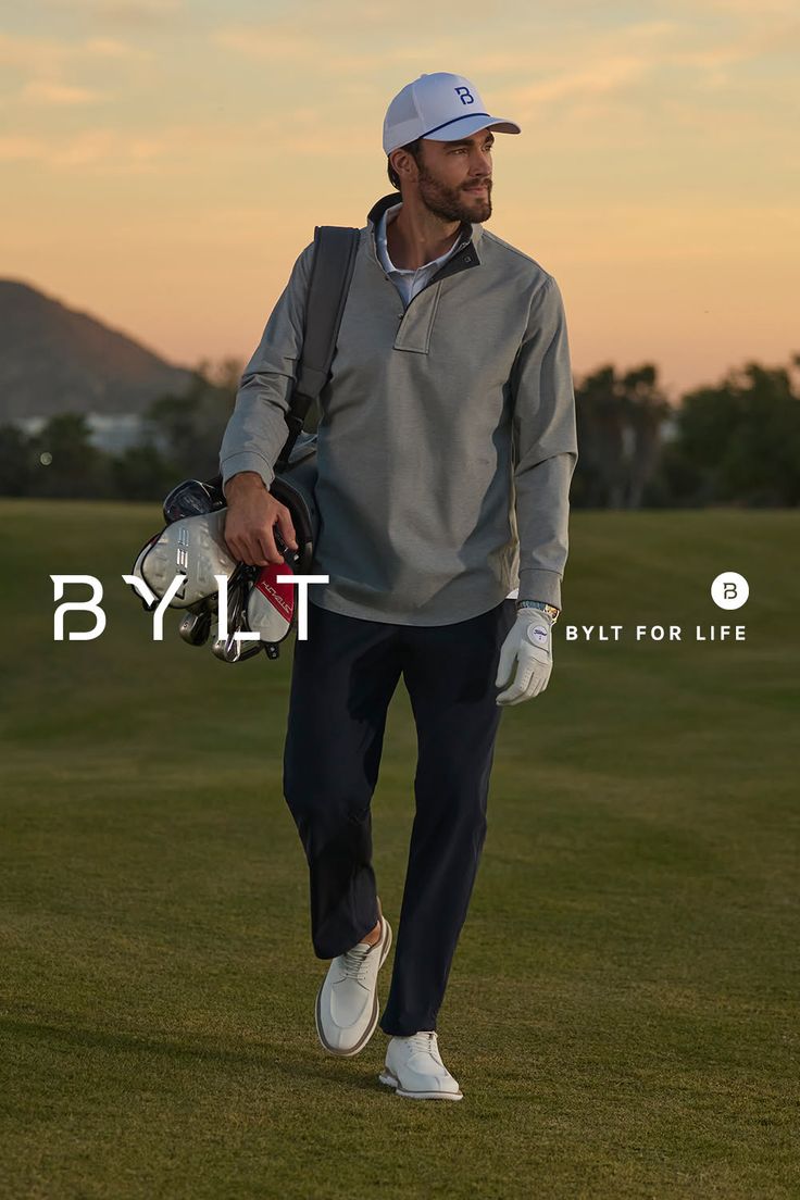 Man in golf attire carrying golf clubs on a golf course at sunset