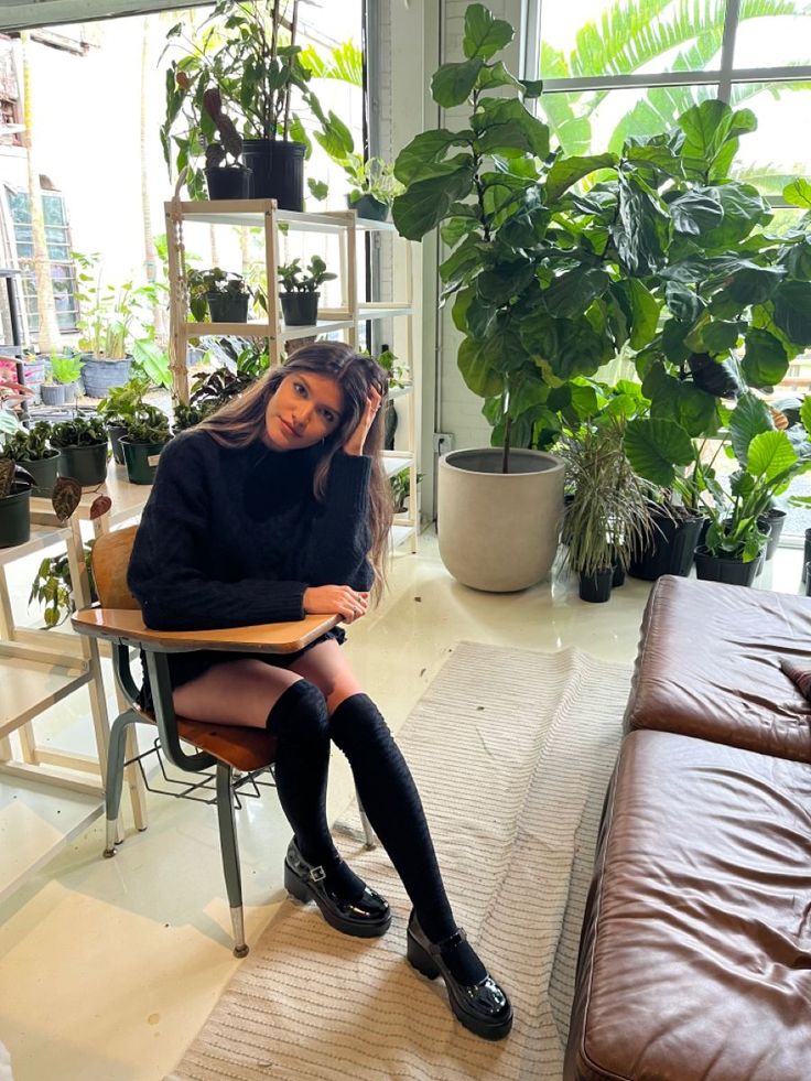 Woman in a black sweater and knee-high socks sitting in a plant-filled room