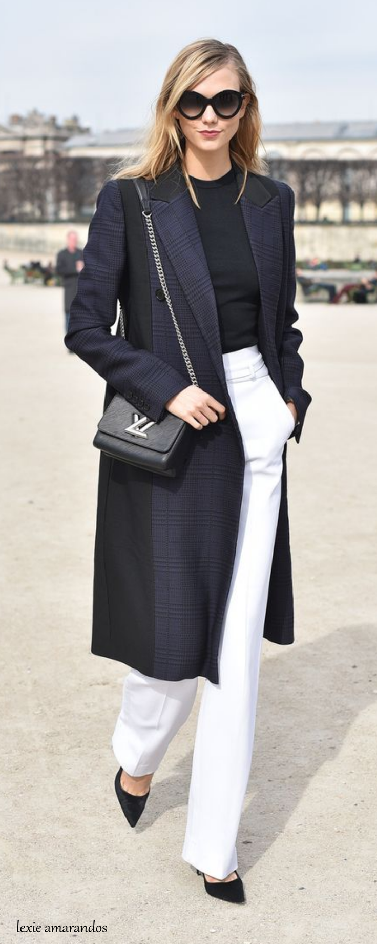 Woman in a long coat, white pants, and sunglasses outdoors