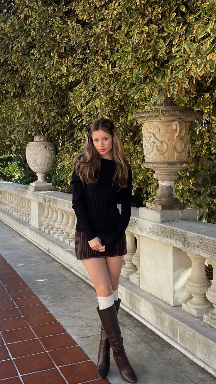 Woman in a black sweater and mini skirt with knee-high boots outdoors