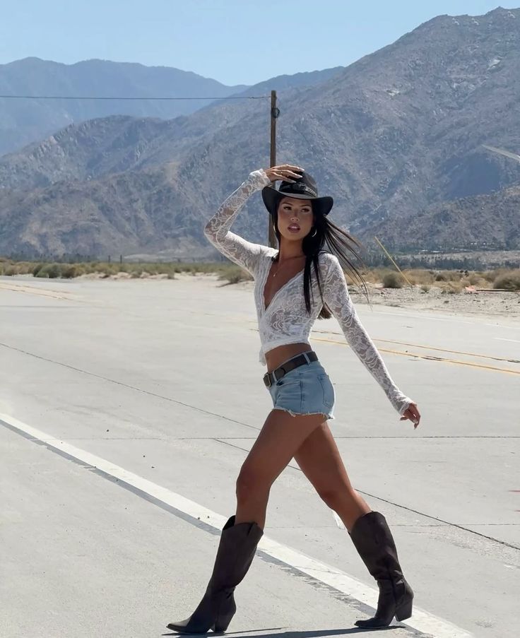 Woman in a cowboy hat, denim shorts, and boots on a desert road