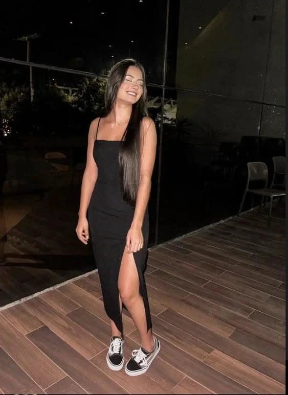 Woman in a black dress with a high slit and sneakers smiling outdoors at night