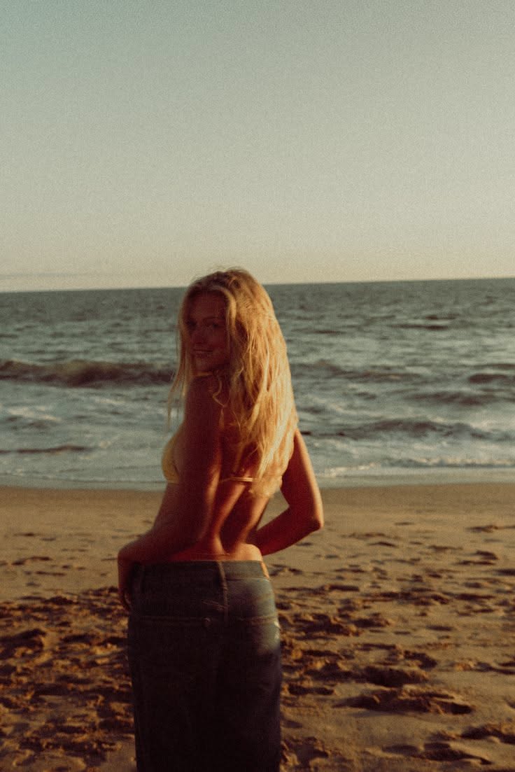 Woman with long blonde hair on a beach at golden hour, looking over her shoulder