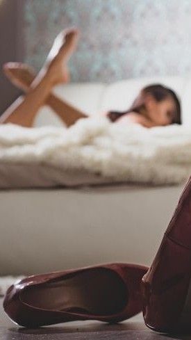 Red heels on the floor with a person lying on a bed in the background