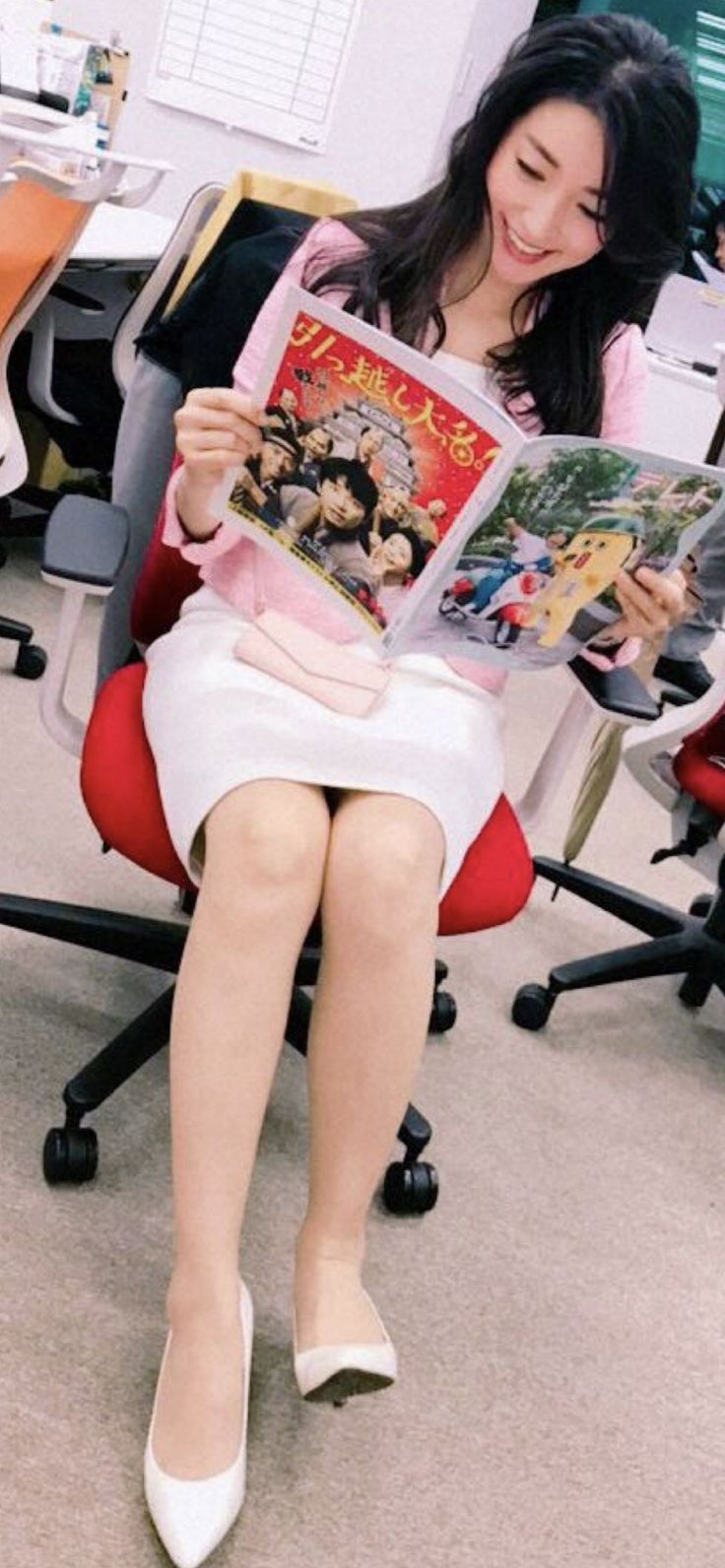 Woman with long dark hair in a pink shirt and white skirt reading a magazine
