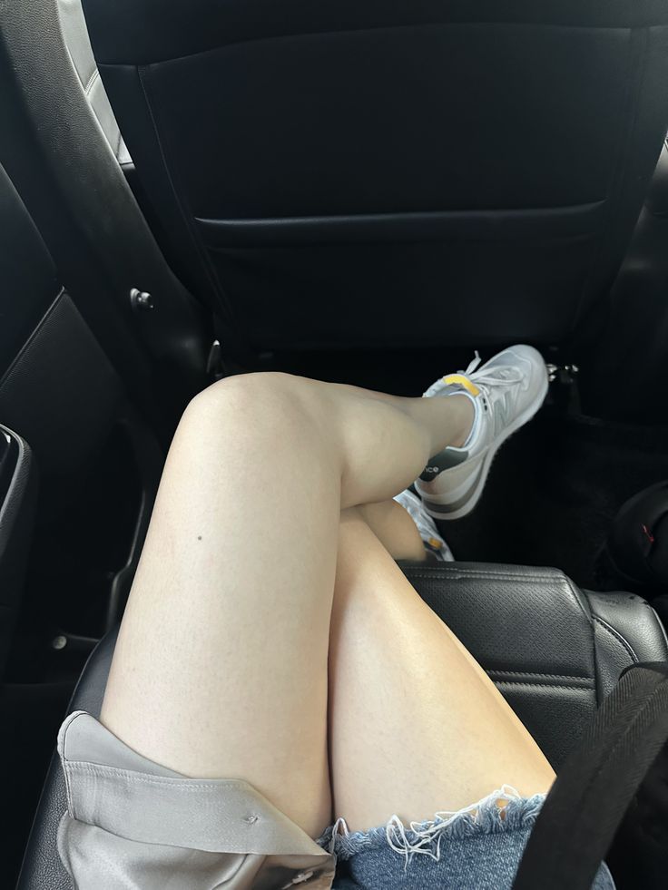 Person's legs in denim shorts and sneakers inside a car