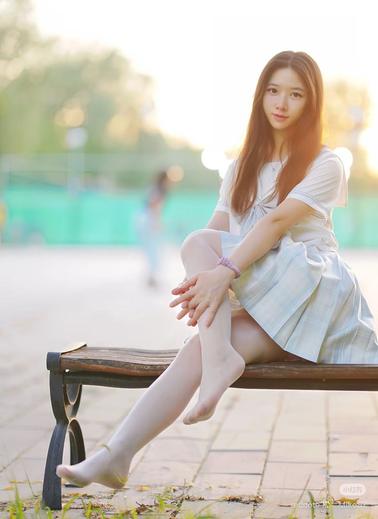 Young woman in a school uniform sitting on a bench during golden hour