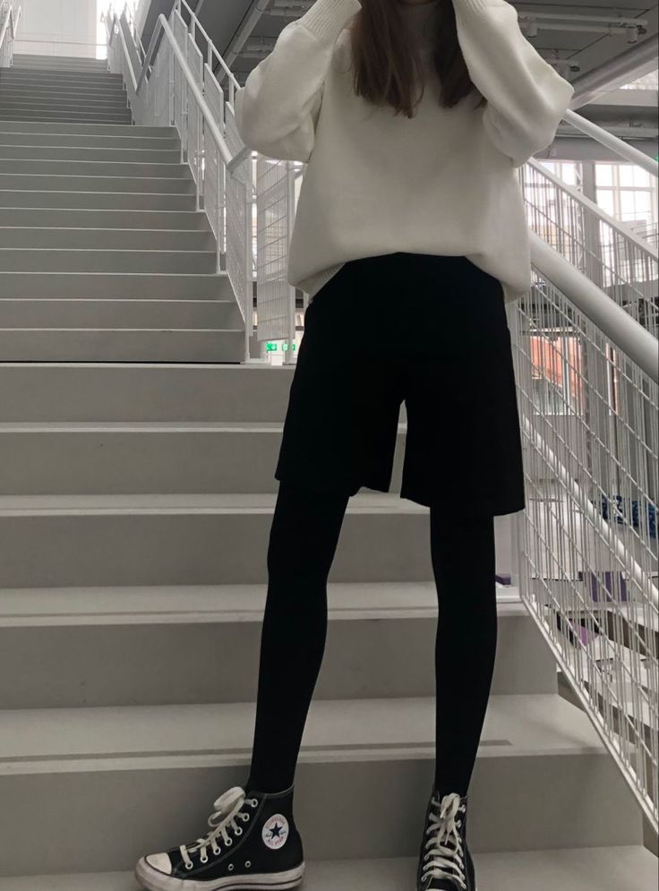 Person in a white sweater, black shorts, and leggings standing on a staircase