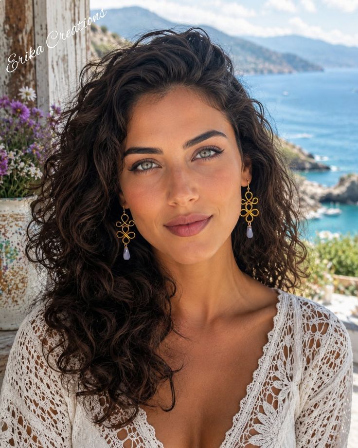 Woman with curly hair wearing a lace top and earrings, with a sea view