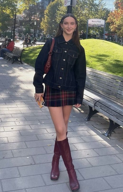 Woman in a denim jacket and plaid skirt standing in a park
