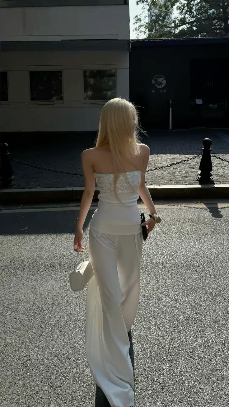 Woman with blonde hair in a white strapless top and pants walking on a street