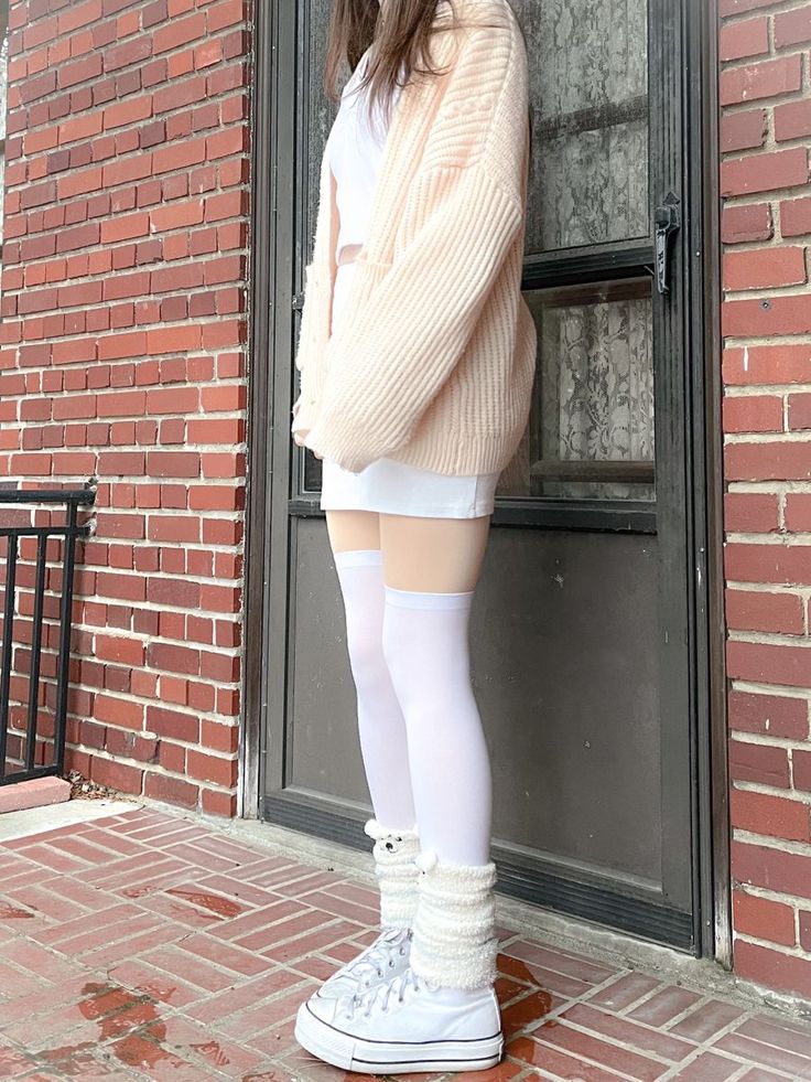 Person in a chunky knit cardigan, white mini skirt, and thigh high socks outdoors