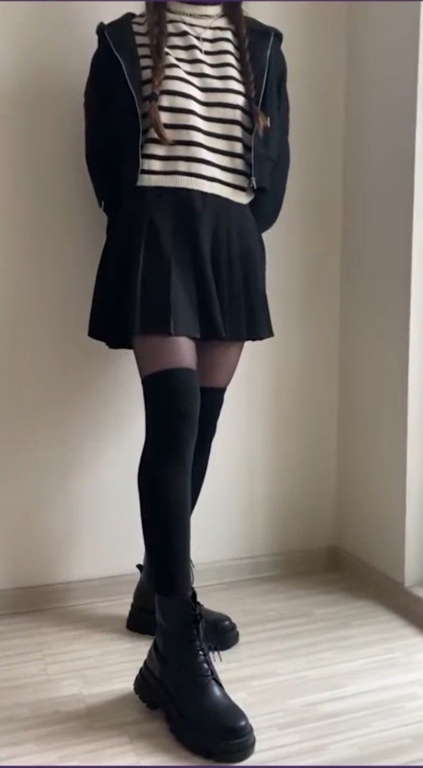 Person in a black skirt, striped sweater, and black boots indoors