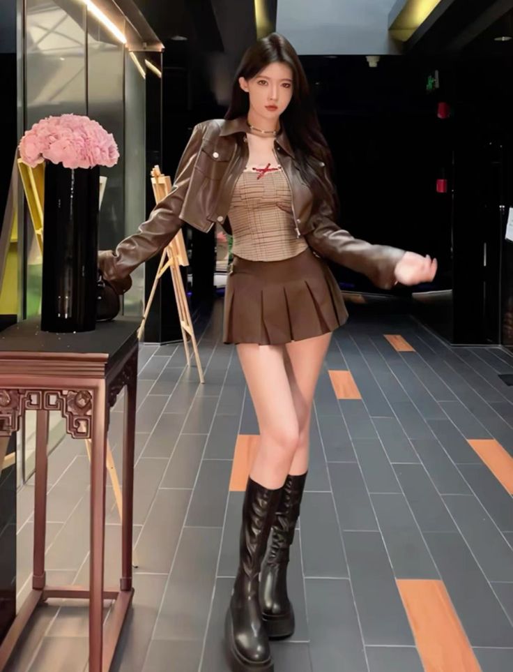 Woman in a brown leather jacket and pleated skirt with knee-high boots indoors