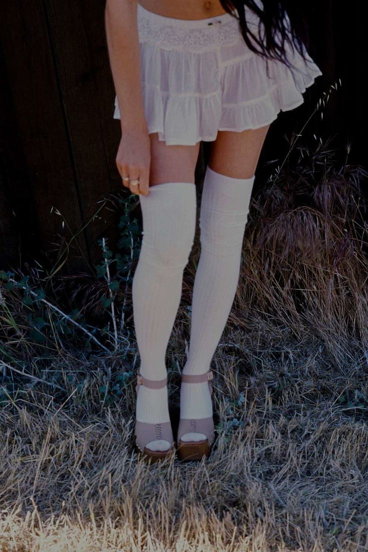 Woman in a white mini skirt and thigh-high socks standing in dry grass