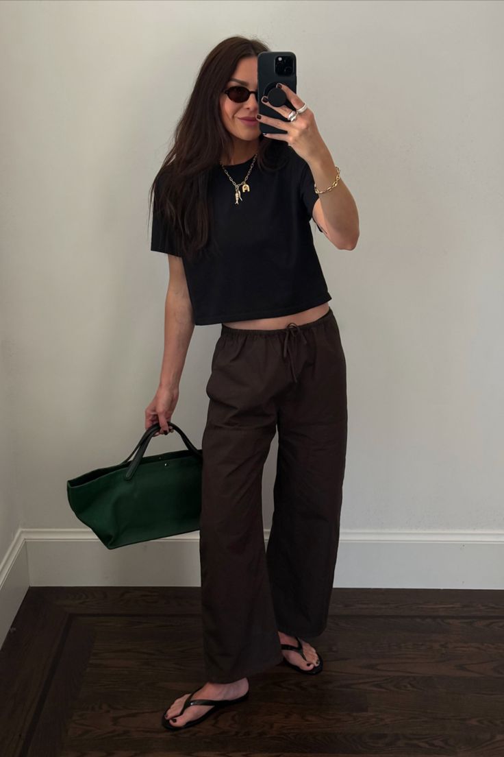 Woman in a black crop top and brown pants taking a mirror selfie indoors