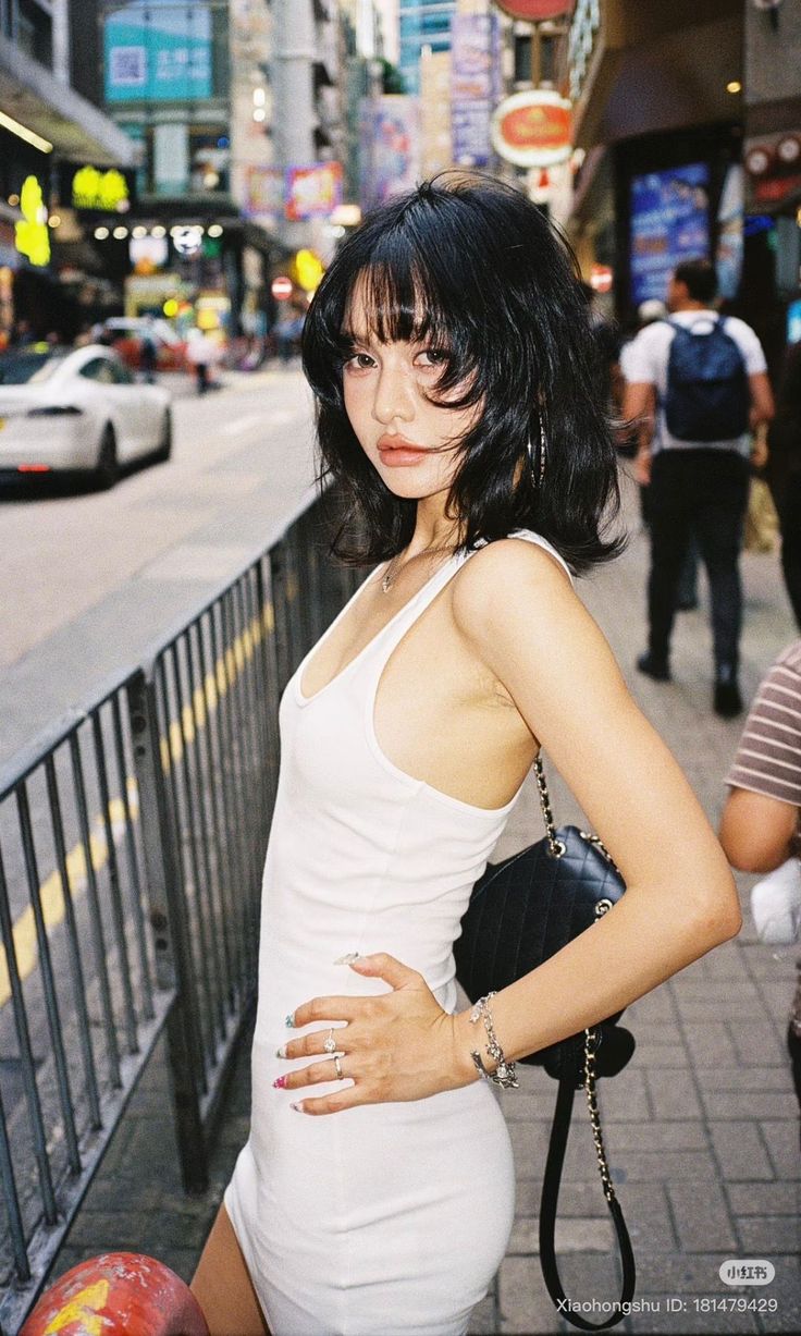 Woman with short black hair in a white tank top on a city street