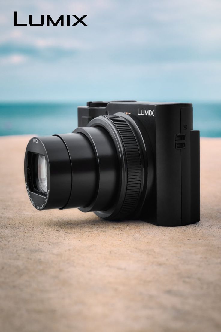 Black digital camera on a sandy surface with the ocean in the background