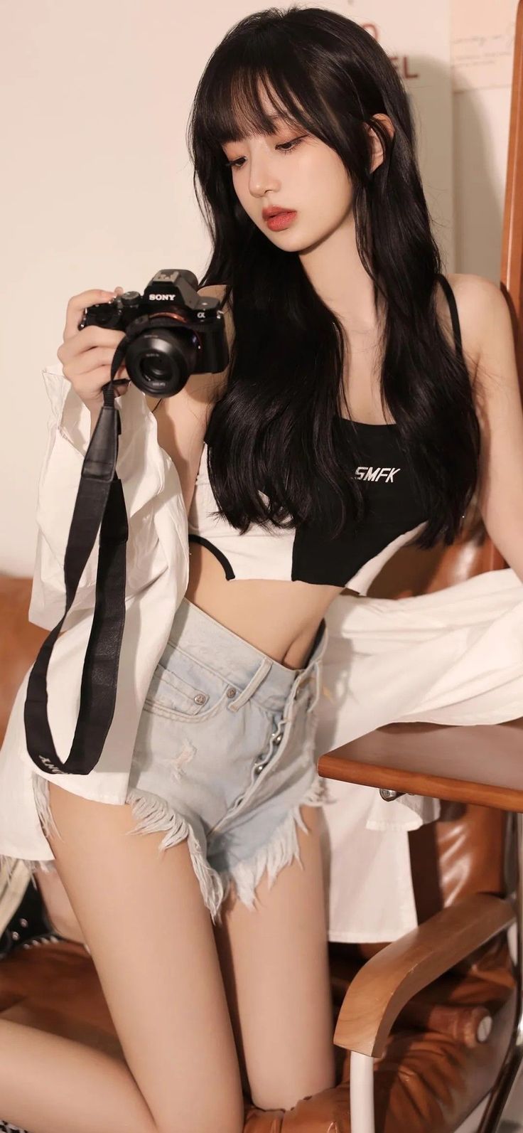 Woman with long black hair in a crop top and denim shorts holding a camera