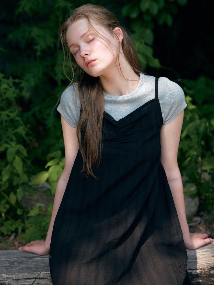 Young woman with long hair and closed eyes wearing a black dress outdoors