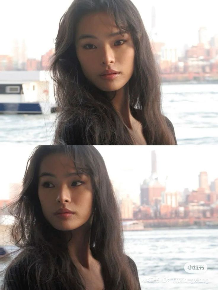 Woman with long dark hair by a waterfront with a cityscape in the background