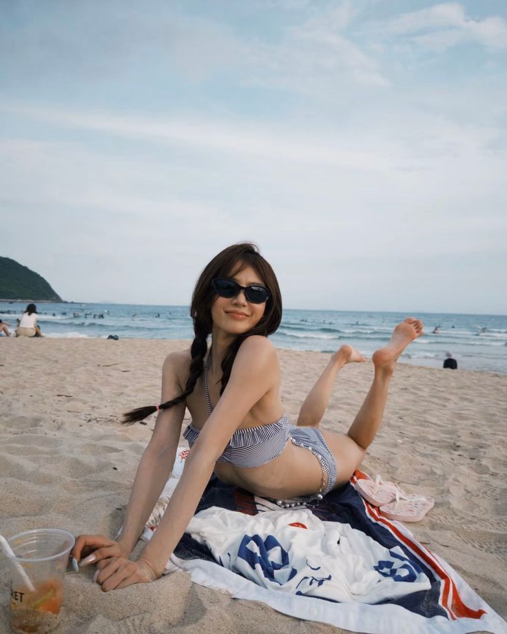 Woman in a striped bikini and sunglasses posing on a beach towel