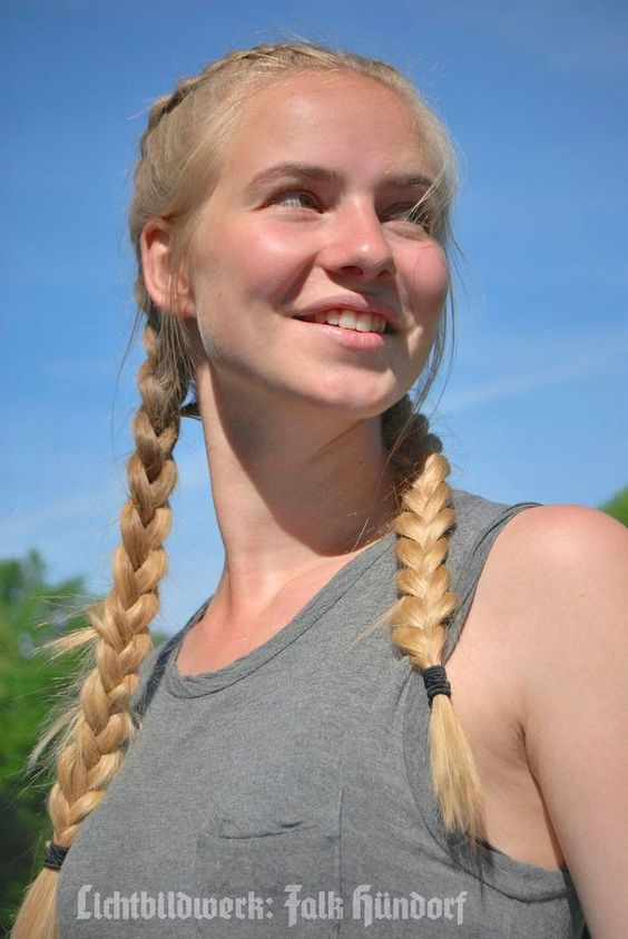 Young woman with blonde braids smiling outdoors under a blue sky