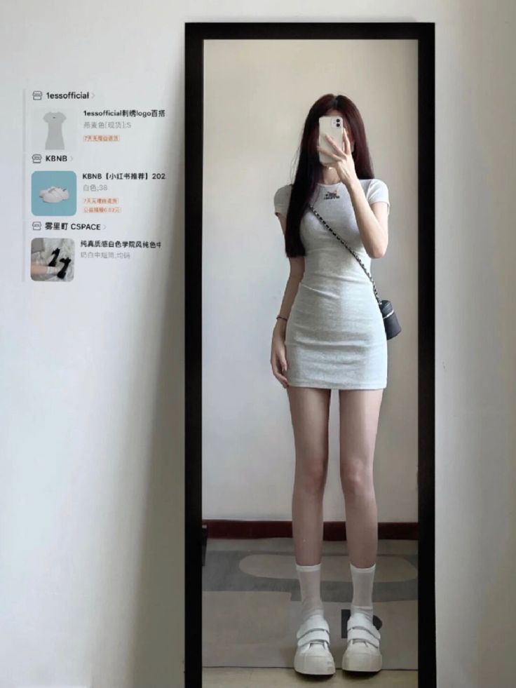 Woman in a short light gray dress taking a mirror selfie