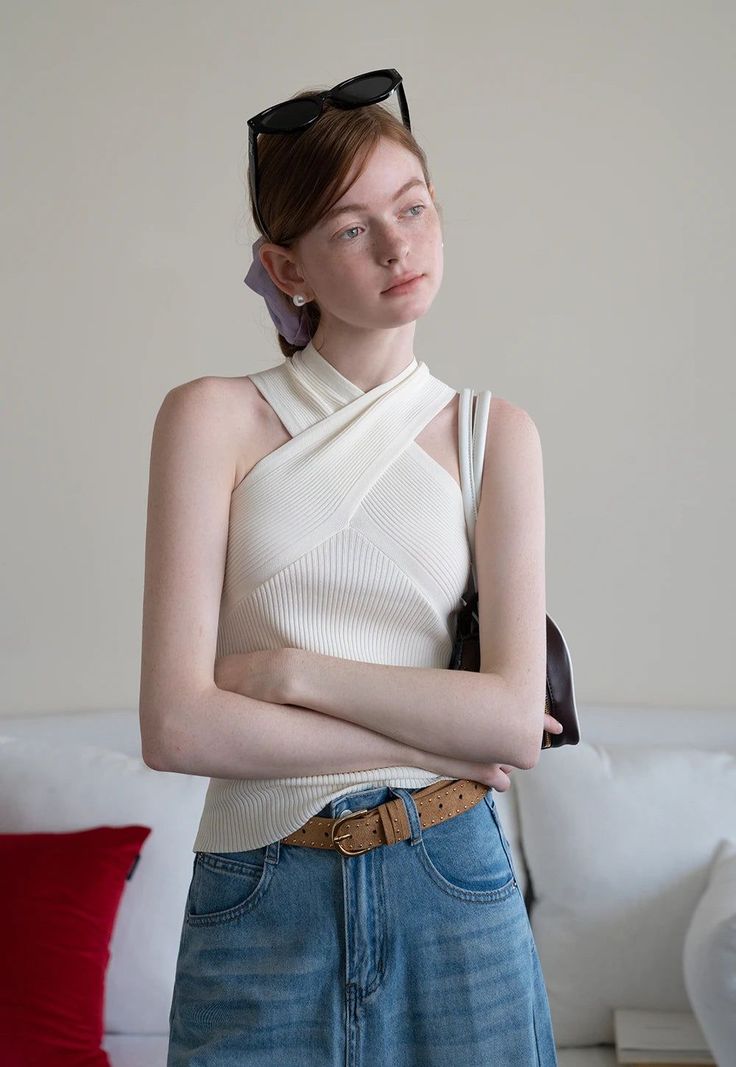 Woman with red hair and freckles wearing a white top and denim skirt indoors