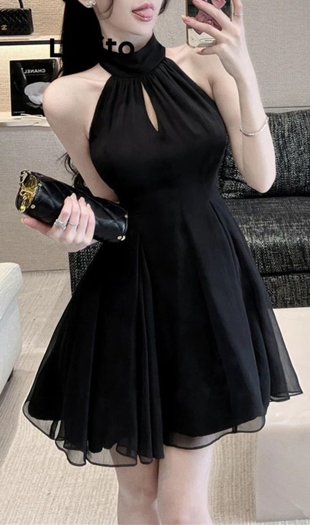 Woman in a black halter neck dress holding a clutch bag indoors