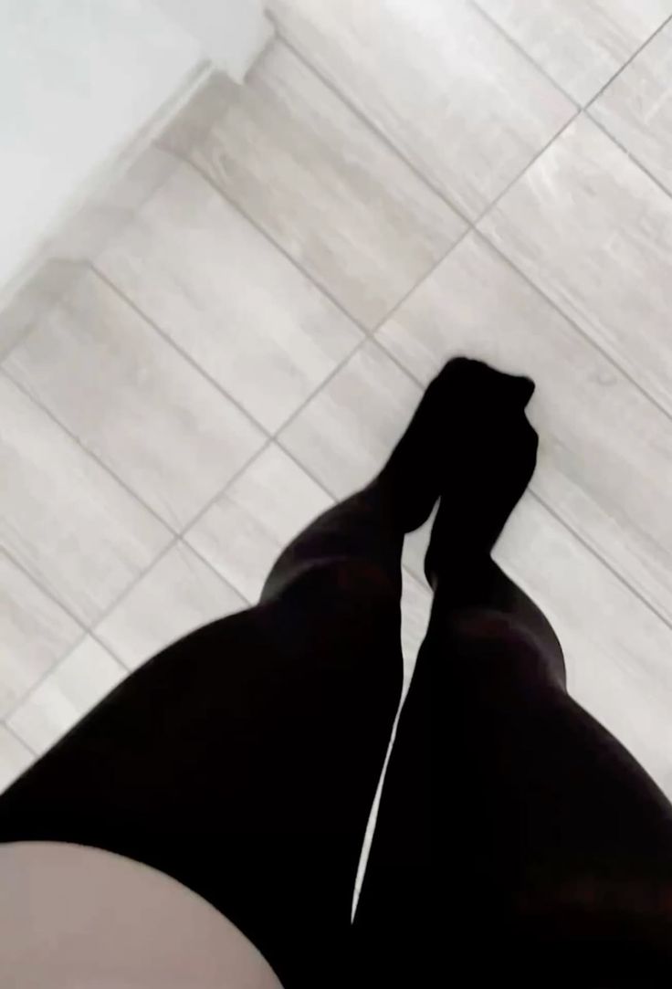 Person wearing black tights standing on a tiled floor from a low angle