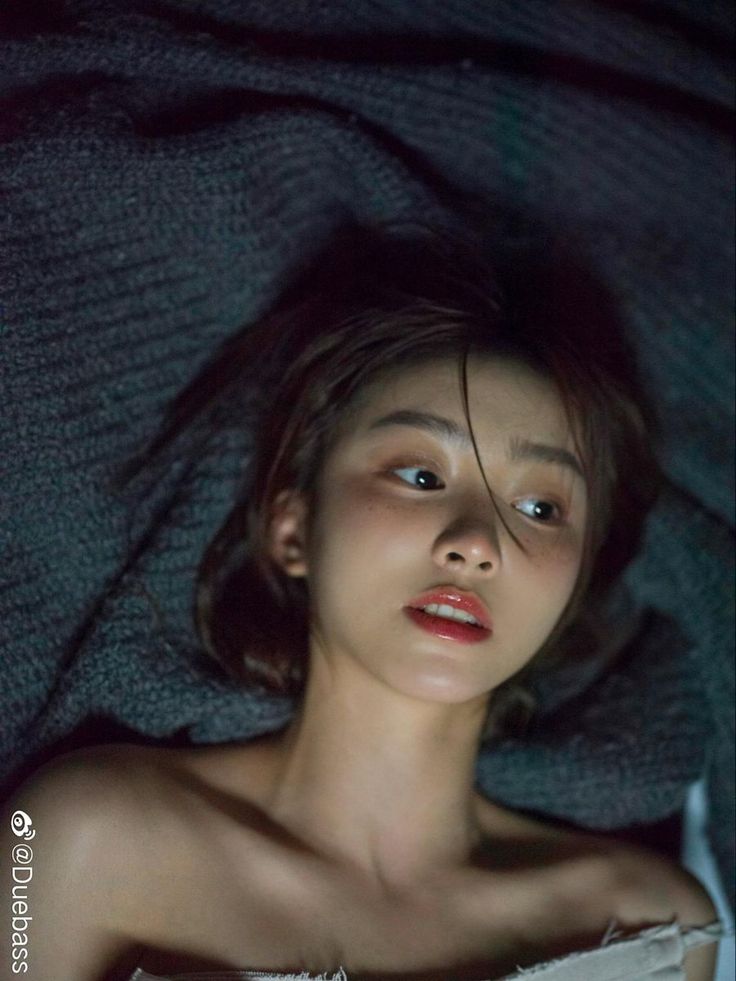 Woman with short hair and exposed shoulders lying on a dark blanket