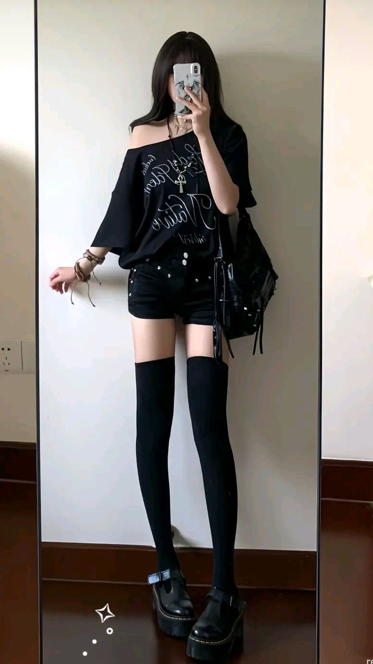 Person in black outfit taking a mirror selfie indoors