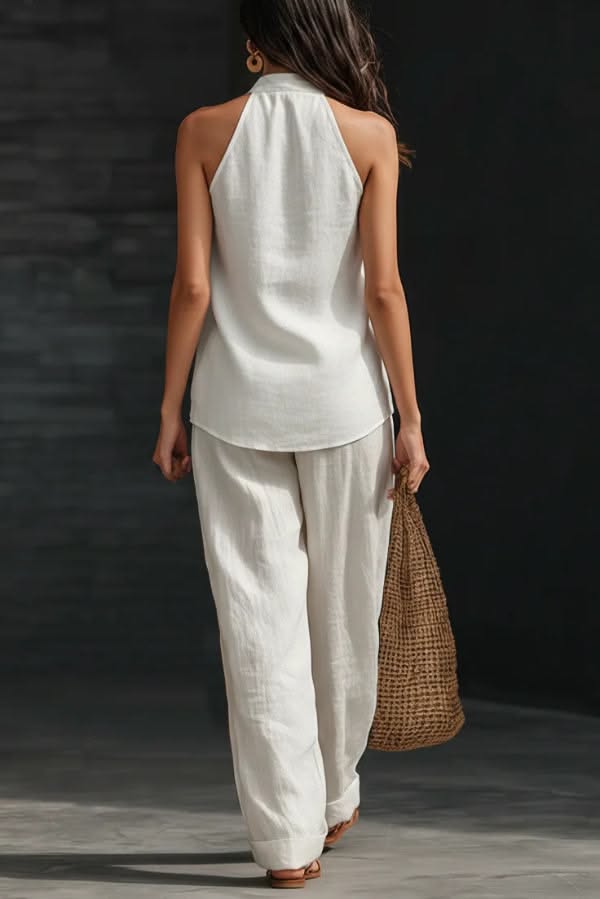 Woman in a white halter top and wide leg pants holding a straw bag