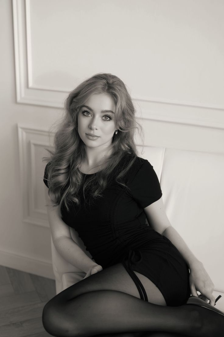 Woman in a black dress and stockings posing on a couch in black and white