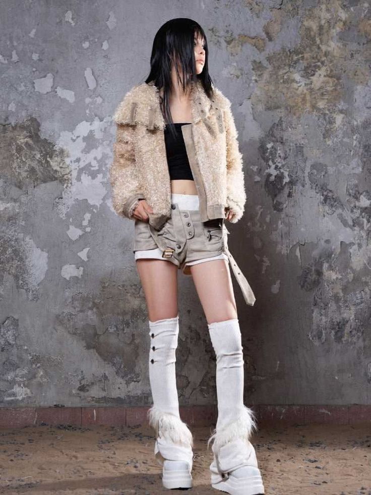Woman in a fur jacket, shorts, and platform shoes against a grungy wall