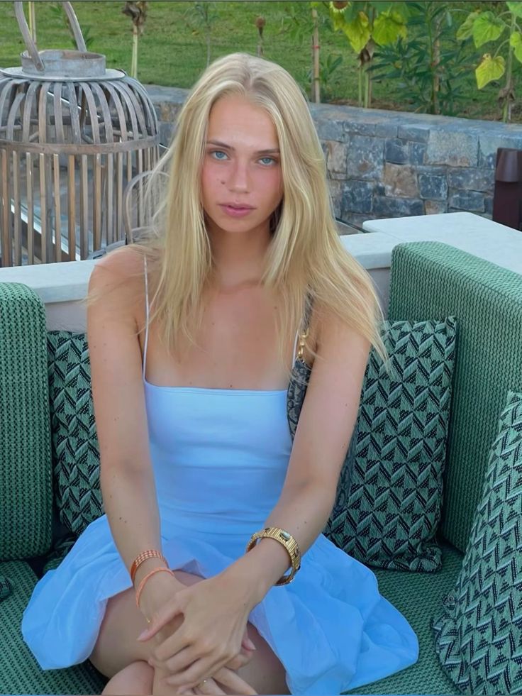 Woman with blonde hair in a blue dress sitting outdoors