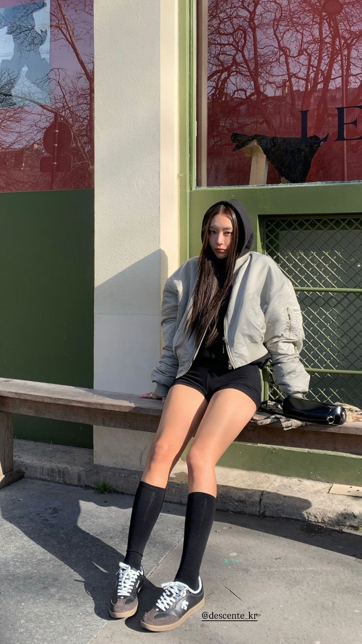 Woman with long hair wearing a hoodie and bomber jacket, sitting outdoors
