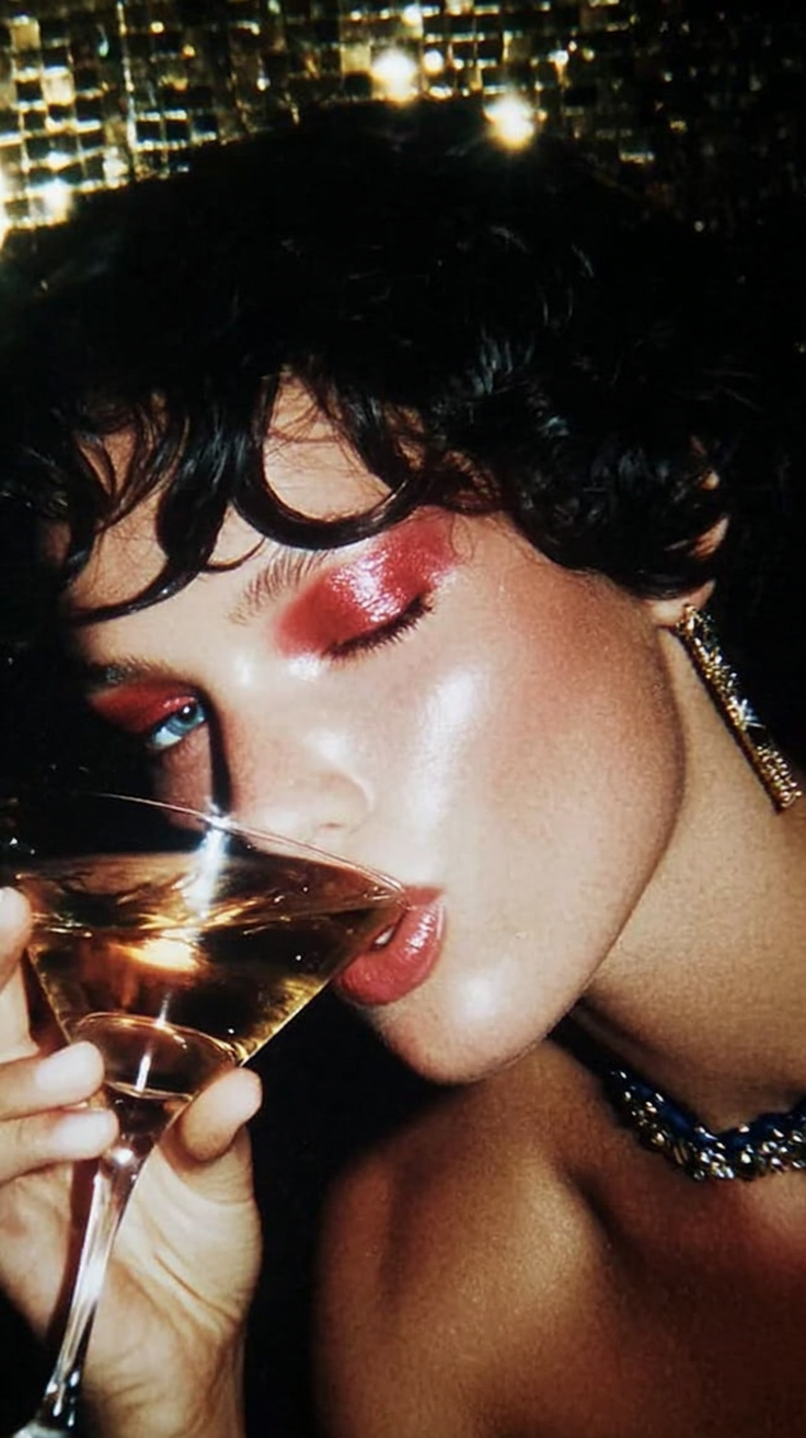 Woman with red eyeshadow drinking from a cocktail glass at night