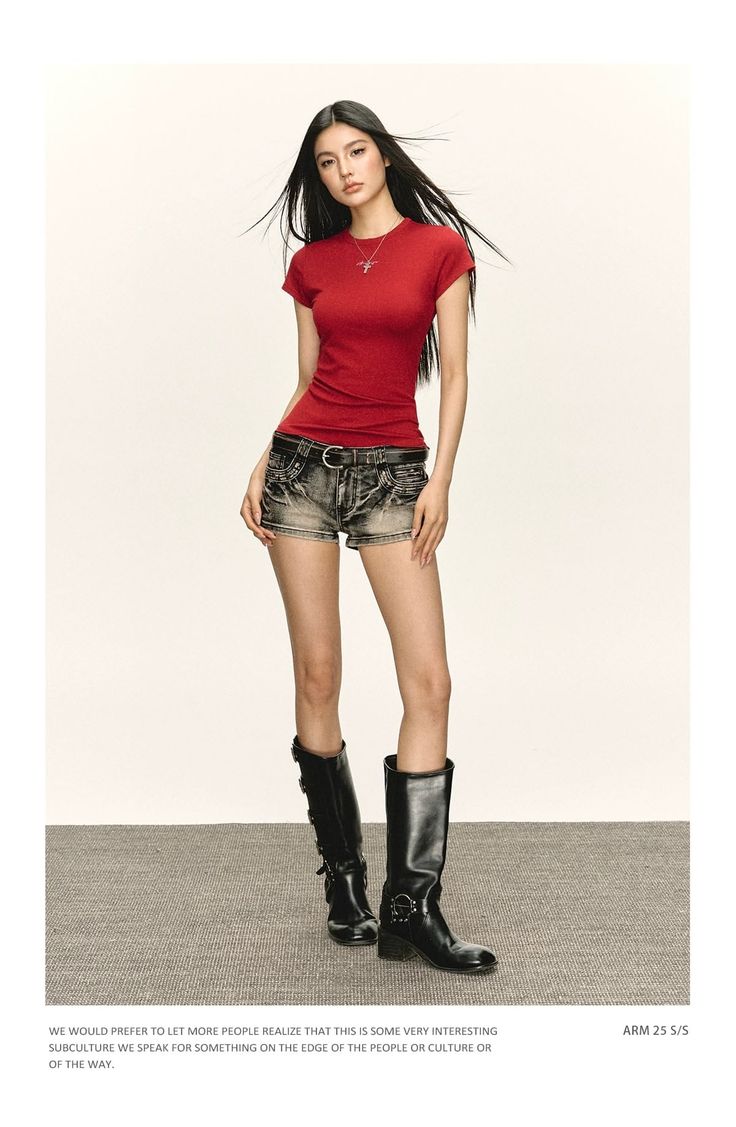 Woman with long black hair wearing a red t-shirt, denim shorts, and black boots
