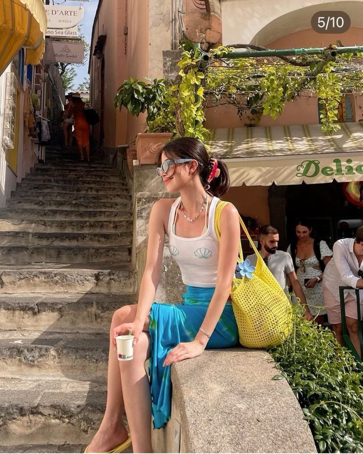 Woman in a white tank top and blue skirt sitting on a stone wall outdoors