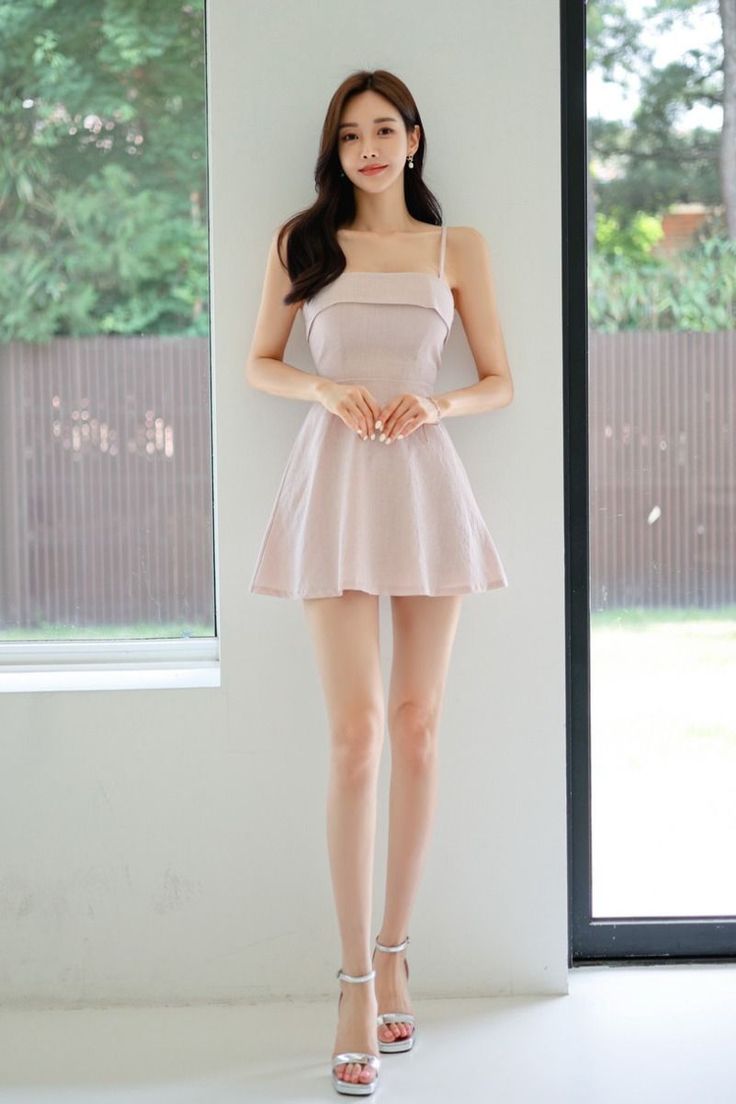 Woman in a pink dress and silver heels standing indoors by a window