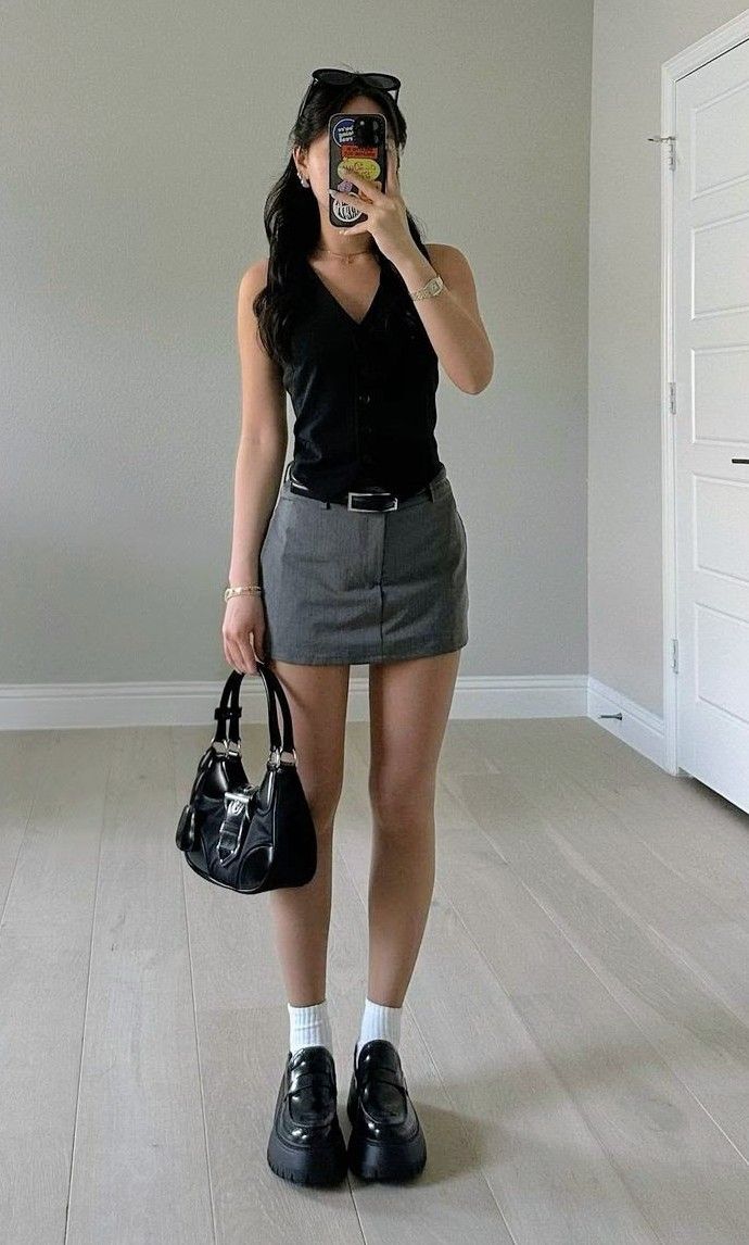 Woman in a black top and mini skirt taking a mirror selfie indoors
