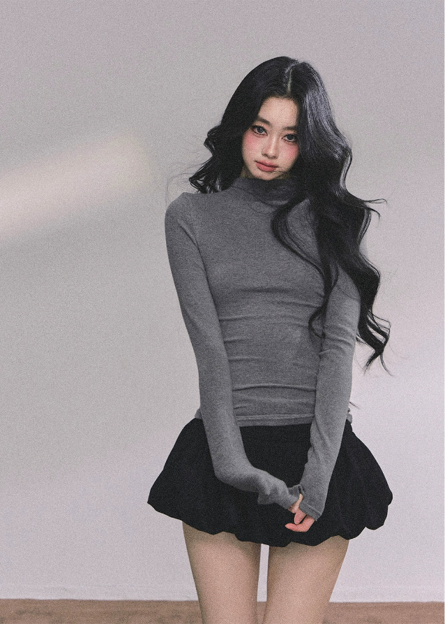 Woman with long black hair wearing a gray turtleneck and black mini skirt indoors