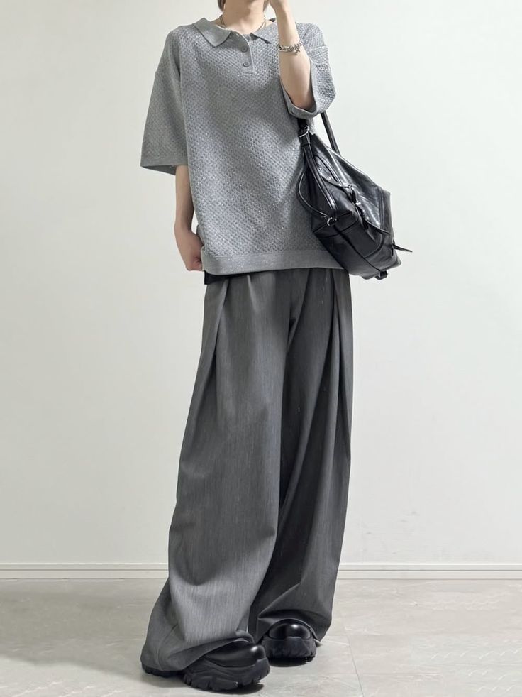 Person in a grey polo shirt and wide leg pants with a black bag