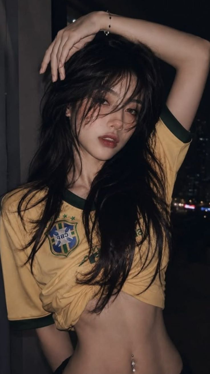 Woman with long dark hair in a yellow shirt with exposed midriff and belly button piercing