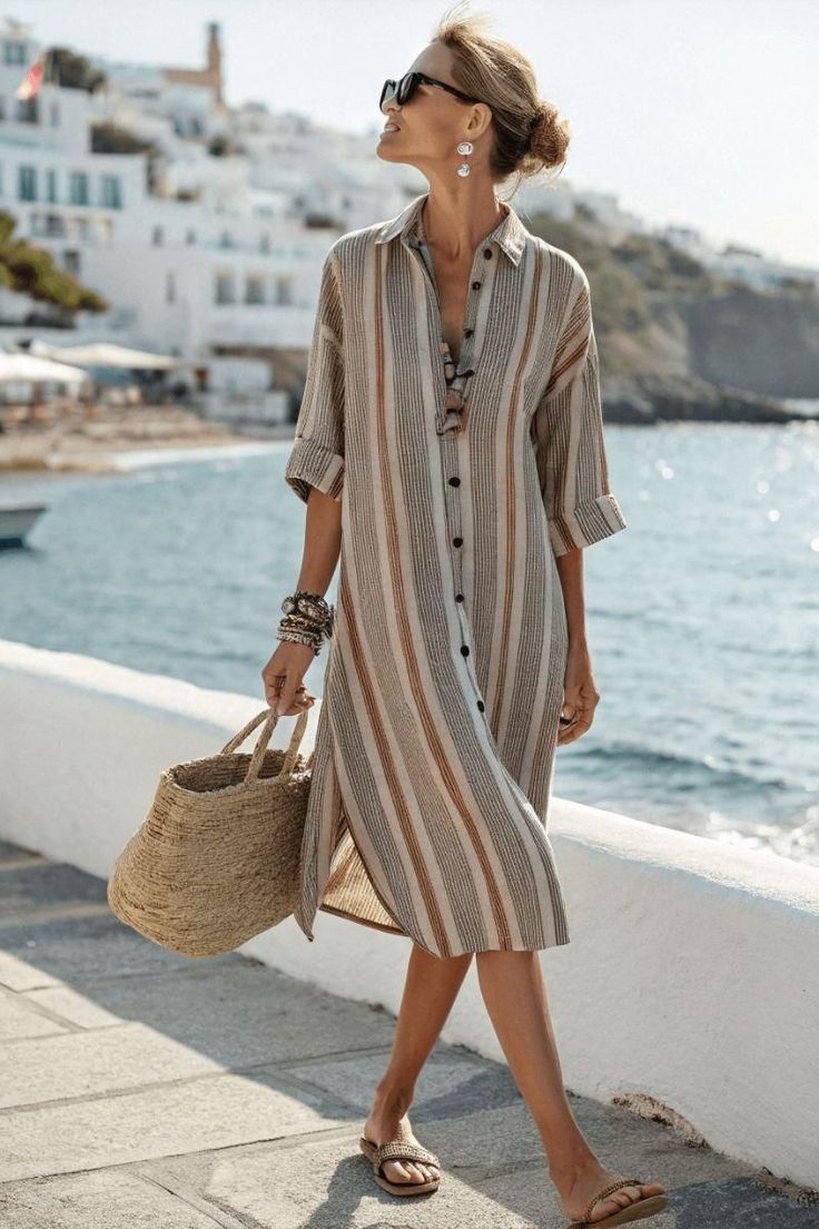 Woman in a striped dress and sunglasses walking along a sunny beachside promenade