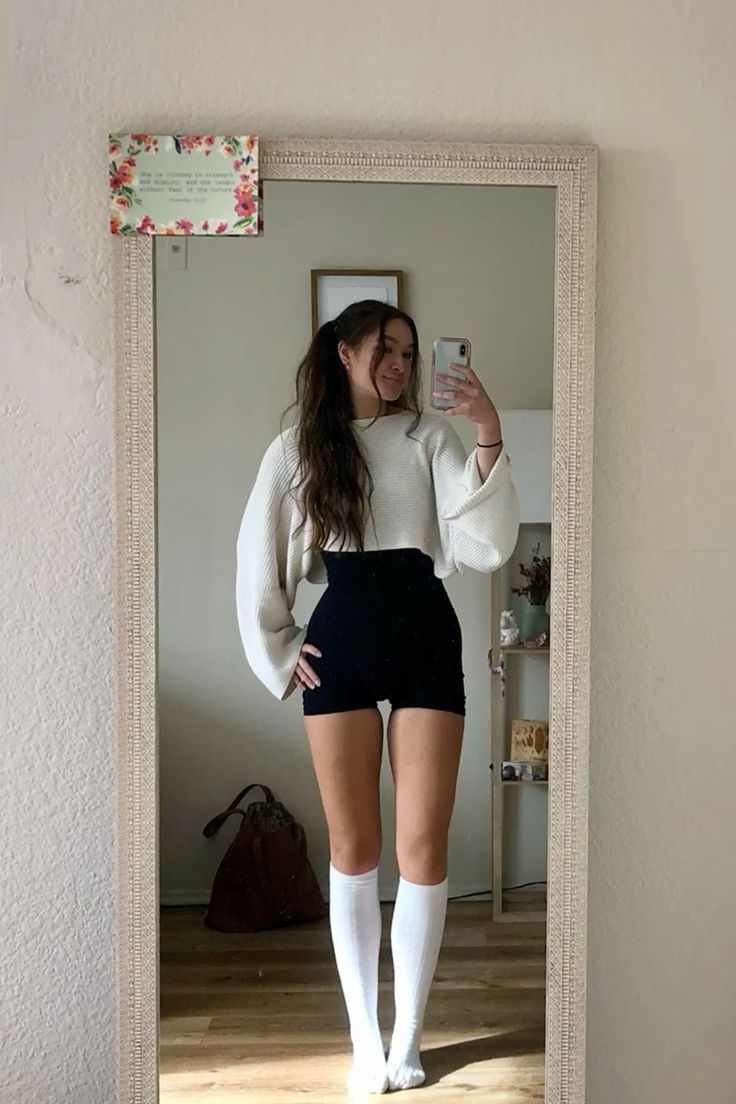 Woman in a cropped sweater and shorts taking a mirror selfie