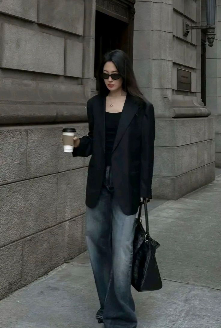 Woman in a black blazer and wide leg jeans walking on a street with a coffee cup